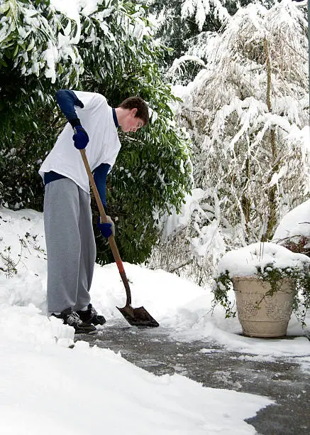 A teen shovels snow from a walkway.