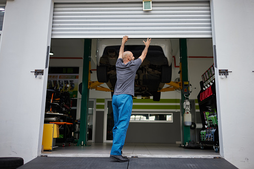 Asian male mechanic starts his day by opening shutter door to car workshop