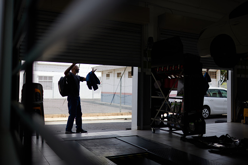 Asian male and female mechanics opening shutter door to car workshop and talking