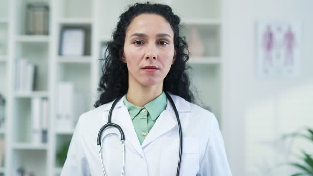 Portrait of serous female doctor pediatrician in white coat with stethoscope looking at camera in modern hospital clinic
