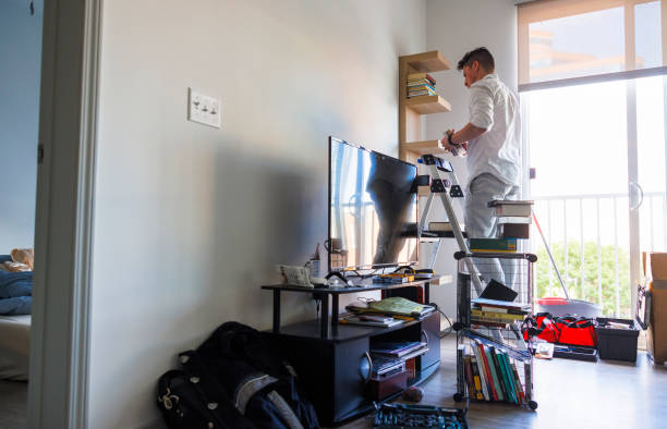 istock Moving in, arranging house space. Hispanic man stand on stepladder putting things in order and unpacking, putting books on the shelf in new apartment 1490560881