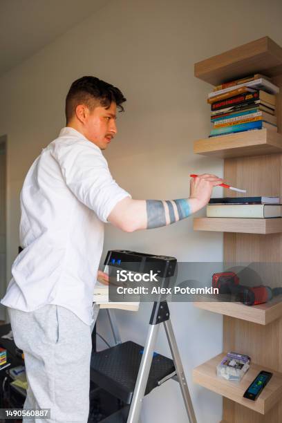 Bookshelf Tidy Up And Keep House Order Latino Man Putting Things In Order Arranging Books On The Shelf Stand On Stepladder In New Apartment Close Up Stock Photo - Download Image Now