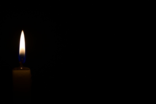 Candle flame burning steadily on a bottom left corner of a frame on a black background