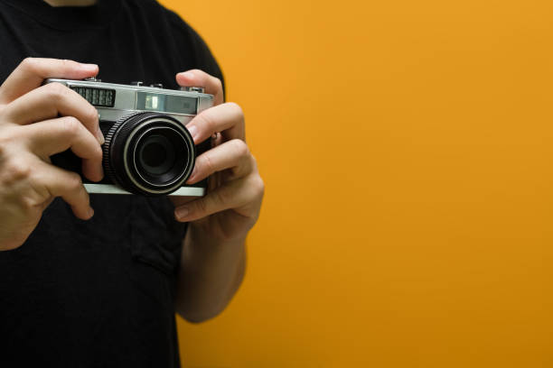 istock Man hands holding retro photo camera on yellow background with copy space. 1490564239