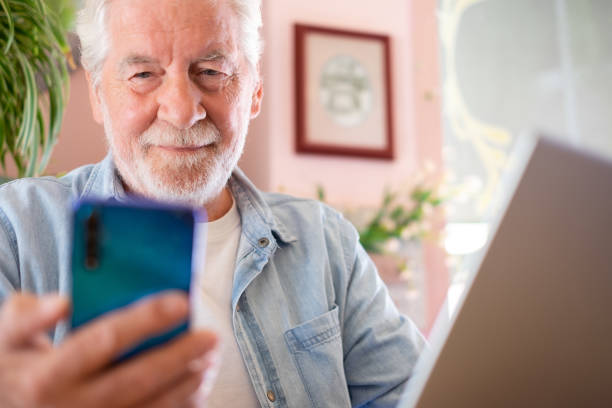 istock Smart work concept. Smiling senior man in coffee shop while working on laptop using mobile phone. Elderly man people enjoying free lifestyle doing job from remote 1490566000