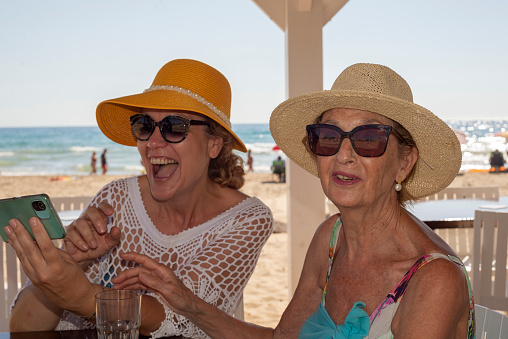 Two older women in hats are using cell phones and smiling at a beach bar by the sea. Summer vacation concept.
Categoría
Estilo de vida
