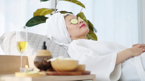 Beautiful woman wearing towel on head laying on spa bed feeling relax with cucumber slices on eyes at spa room. Spa aromatherapy concept