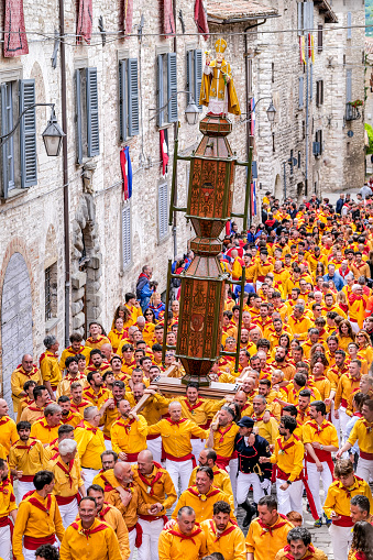 Gubbio, Umbria, Italy, May 15 -- A scene of the traditional and ancient Festa dei Ceri in the historic heart of the medieval town of Gubbio in Umbria. The celebration consists of a race of three wooden columns weighing almost 300 kg each, called Ceri, carried on the shoulders of dozens of bearers, on top of which are placed the statues of Sant'Ubaldo (Saint Ubaldo) protector of Gubbio, San Giorgio (Saint George) and Sant'Antonio Abate (Saint Anthony). The race develops along the streets and alleys of Gubbio up to the summit of Monte Ingino where the Basilica of Sant'Ubaldo is located. This religious celebration, much loved by the whole community of Gubbio, is considered one of the oldest in Italy and in the world and its origins date back to the 12th century. In the photo: The Cero of Sant'Ubaldo runs through the stone alleys of Gubbio carried on the shoulders of dozens of bearers called Ceraioli. Image in high definition quality.