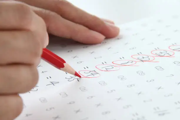 Teahcer's hand checking math test sheet with red pencil