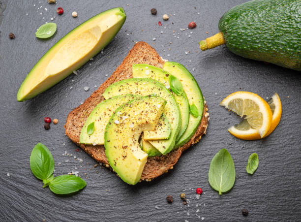 istock Avocado toast - bread with avocado slices on natural slate serving board. Top view. 1490577115