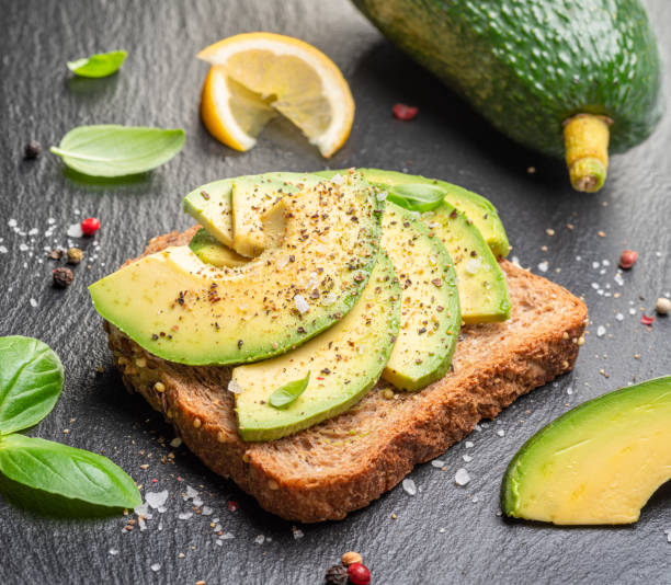 istock Avocado toast - bread with avocado slices on natural slate serving board. Top view. 1490577134