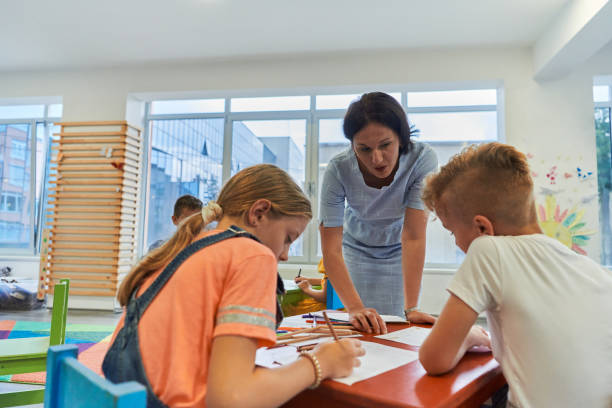 istock Creative kids during an art class in a daycare center or elementary school classroom drawing with female teacher. 1490577327