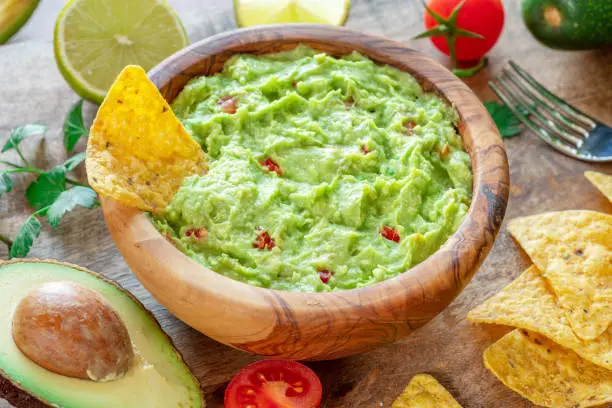 Guacamole, guacamole ingredients and chips on wooden background.