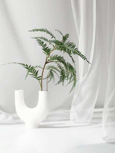 Empty white counter table, soft smooth blowing sheer cloth drapery, green tropical fern in modern ceramic vase in sunlight