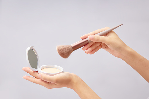 A compact powder placed on female hand model with a powder brush is held on another hand. Minimal white background. Branding mockup