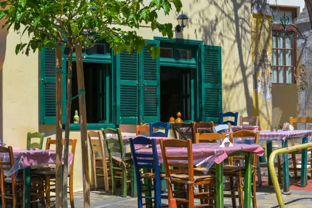 Rustic Mediterranean tavern or casual street restaurant with different painted wooden chairs at the tables in front of the windows of a traditional house in the old town Thessaloniki, Greece