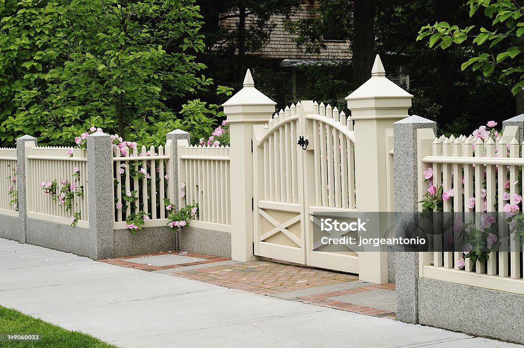 Elegant gate and fence on house entrance Elegant gate and fence on house entrance. Wood, granite, brick. Pink rose bushes coming out to sidewalk through off white posts. Gate Stock Photo