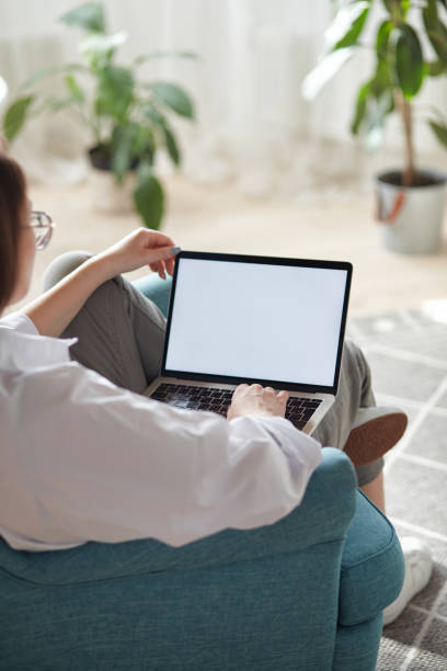 istock Mockup white screen laptop woman using computer sitting on armchair at home, back view, focus on screen 1490601162