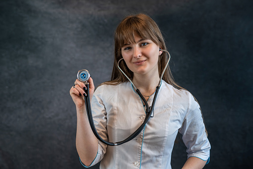 Portrait of female general practitioner or doctor with stethoscope isolated on dark, coronavirus pandemic concept. Medical personal