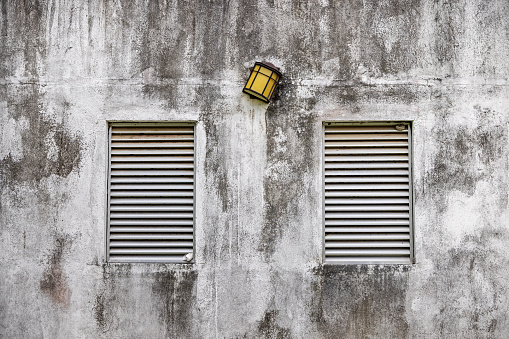 Two blinded windows and a lamp on a dirty white wall om Trincomalee in Sri Lanka