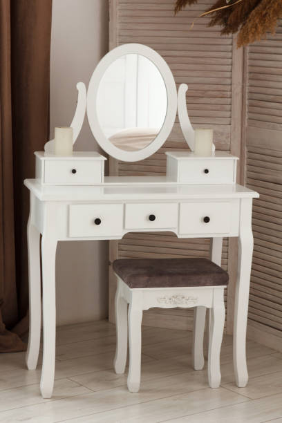 White dressing table with oval mirror and chair is part of cosy interior of beautiful contemporary bedroom stock photo