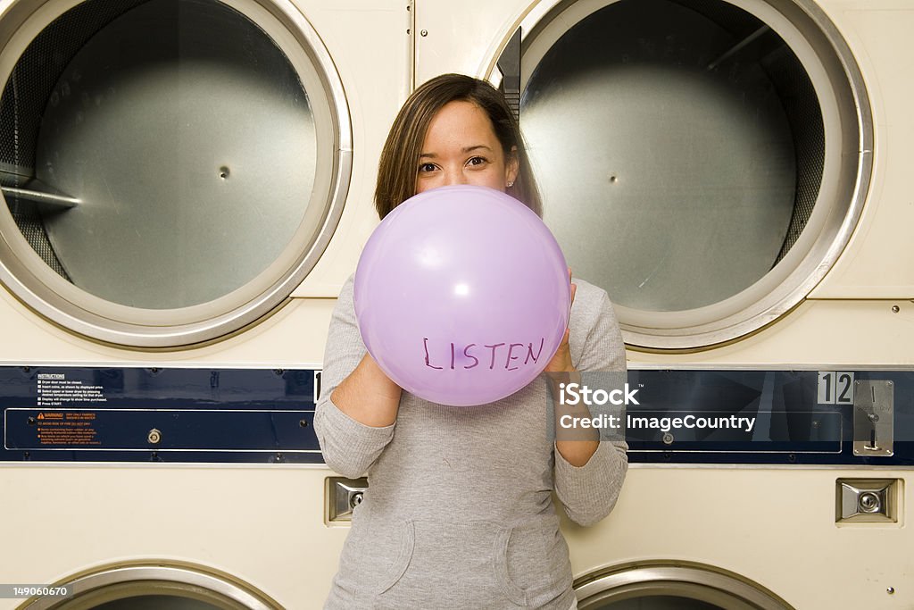 Young women blowing up a balloon at the laundromat. Young women blowing up a balloon with the word "LISTEN" on it. Adult Stock Photo