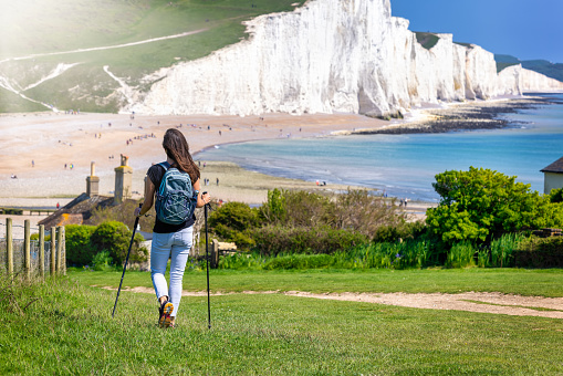 A woman hikes over green fields at the Seven Sisters Cliffs in Sussex, England, during a sunny spring day