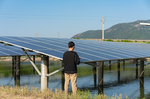 Solar panels are installed above the fish farm, and the technician holds a tablet computer to check and record the power generation of the solar panels