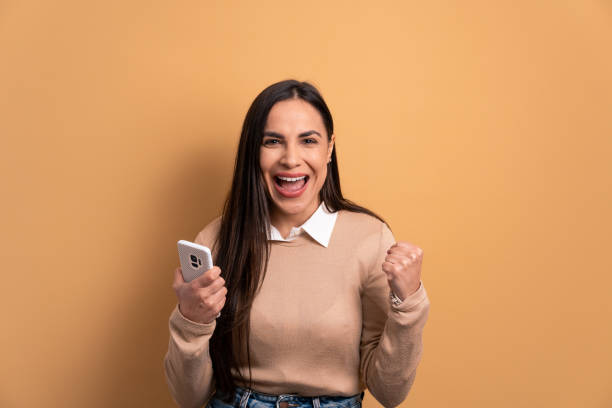 istock woman raising arms and celebrating in beige studio background. 1490612277