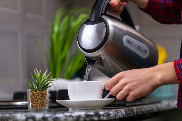 Person brews tea using boiling water from an electric kettle in kitchen at home. Time for breakfast
