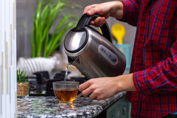 istock Person brews tea using boiling water from an electric kettle in kitchen at home 1490614748