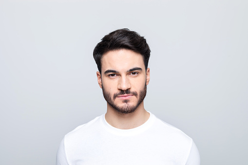 Handsome man wearing white t-shirt looking at camera. Studio shot, grey background.