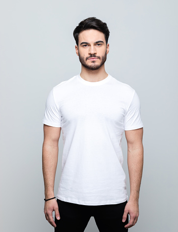 Handsome man wearing white t-shirt looking at camera. Studio shot, grey background.