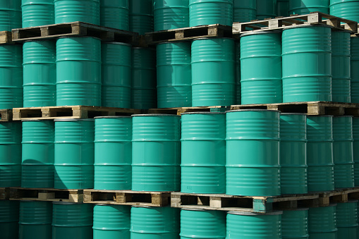Pile of green industrial barrels stored outside a warehouse.