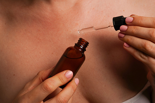 woman holds brown bottle with cosmetic oil in hands against her body, natural skin care products