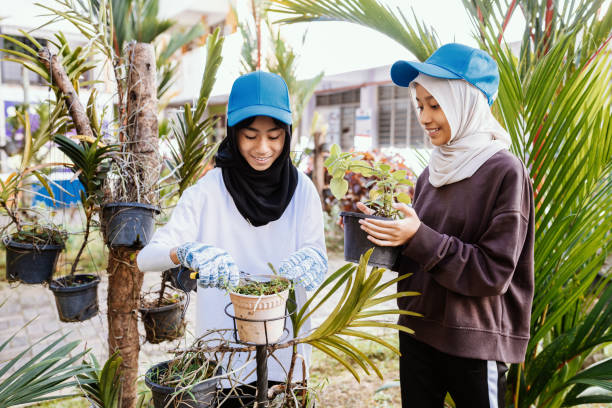 Two happy female teenagers of different nationalities and faiths in the park after training. Caucasian girl in the foreground. A Muslim teen in a hijab and a green sweater smiles and poses in nature.