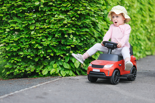 toyYoung toddler laughing as she zooms down a residential path sitting on a toy car