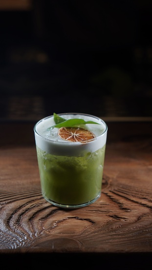 A vertical shot of an iced matcha lemonade with a slice of orange in a glass