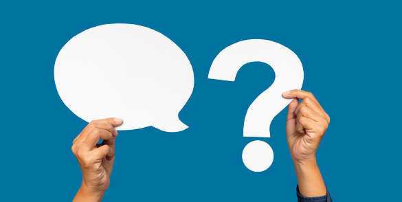 A speech bubble and question mark symbol concept. Hand holding a blank white speech bubble and a white question mark against a blue background. Space for text. Close-up photo.