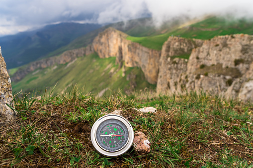 On the ground a compass with a view of the mountain during the day