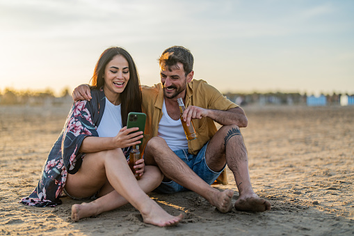 Young couple uses mobile phone while sitting on the beach