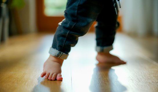 Close-up of baby boy taking his first steps on wooden floor. Toddler learning how to walk, First steps