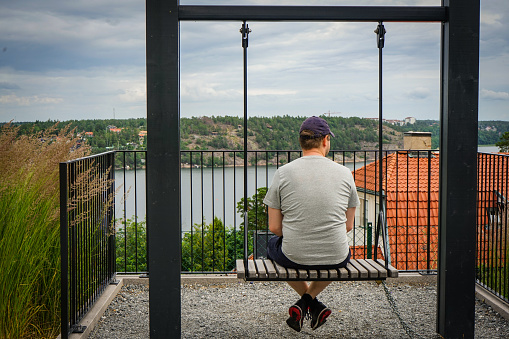 Rear view of man sitting on swing against sky