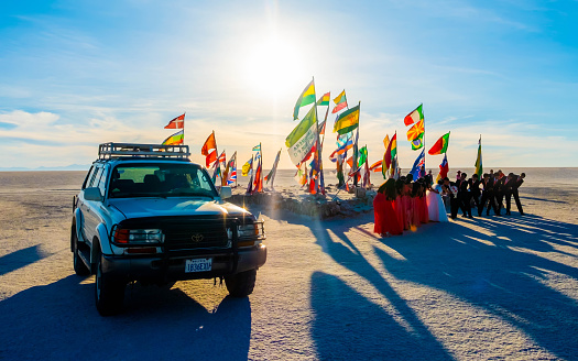 Salar de Uyuni, Bolivia - 21 October 2018: People celebrating near sunshine place with flags and car at foreground