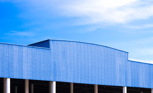Blue Corrugated metal Roof of large Industrial Warehouse Building against blue sky Background in Perspective side view