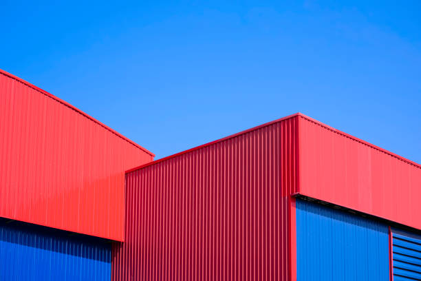 rote und blaue wellblechlagergebäude im modernen stil vor blauem himmelshintergrund - architecture roof aluminum sheet industry stock-fotos und bilder