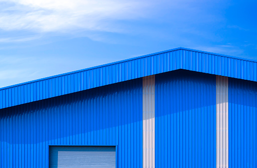 Blue corrugated metal warehouse and white stripes with automatic roller shutter door against blue sky background