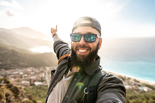 Happy tourist taking selfie against picturesque view of sea and mountains at sunset, standing on the top.