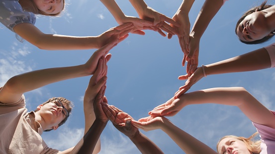 Bottom view of group of high school students raise the shape of a circle created from their palms. Classmates stand together and make hands circle outdoors