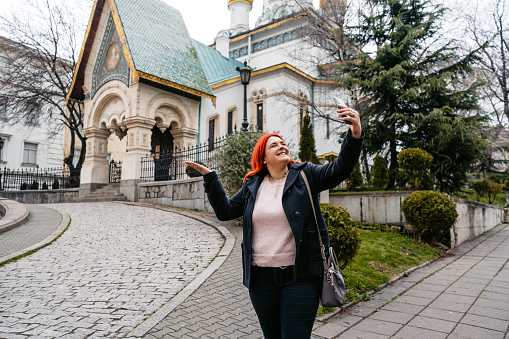 Young plus size woman having a video call in front of the Church of St Nicholas the Miracle-Maker (Russian Church) in Sofia, Bulgaria.